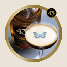Espresso-style cocktail with a blue butterfly on its foam in front of a Licor 43 bottle, framed in a gold circle with the Licor 43 logo.